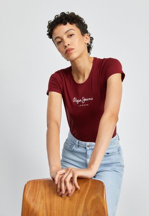 T-shirt ajusté bordeaux à manches courtes avec le logo blanc "Pepe Jeans London", associé à un jeans taille haute bleu clair. Texture de tissu lisse.
