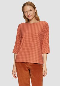Gestreepte oranje top met brede halslijn en driekwart mouwen, gemaakt van zachte stof, gecombineerd met roestkleurige corduroy broek.