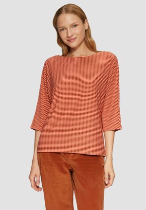 Gestreepte oranje top met brede halslijn en driekwart mouwen, gemaakt van zachte stof, gecombineerd met roestkleurige corduroy broek.