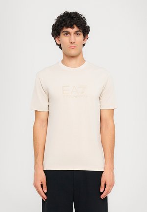 Beige short-sleeve t-shirt made of soft cotton. Features a subtle EA7 logo in a slightly darker shade on the front. Simple design and round neckline.