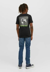 Svart bomulls t-shirt med en grafik av en jordglob på baksidan med texten "BÄTTRE VÄRLD" i grönt, kombinerad med blå jeans och sneakers.