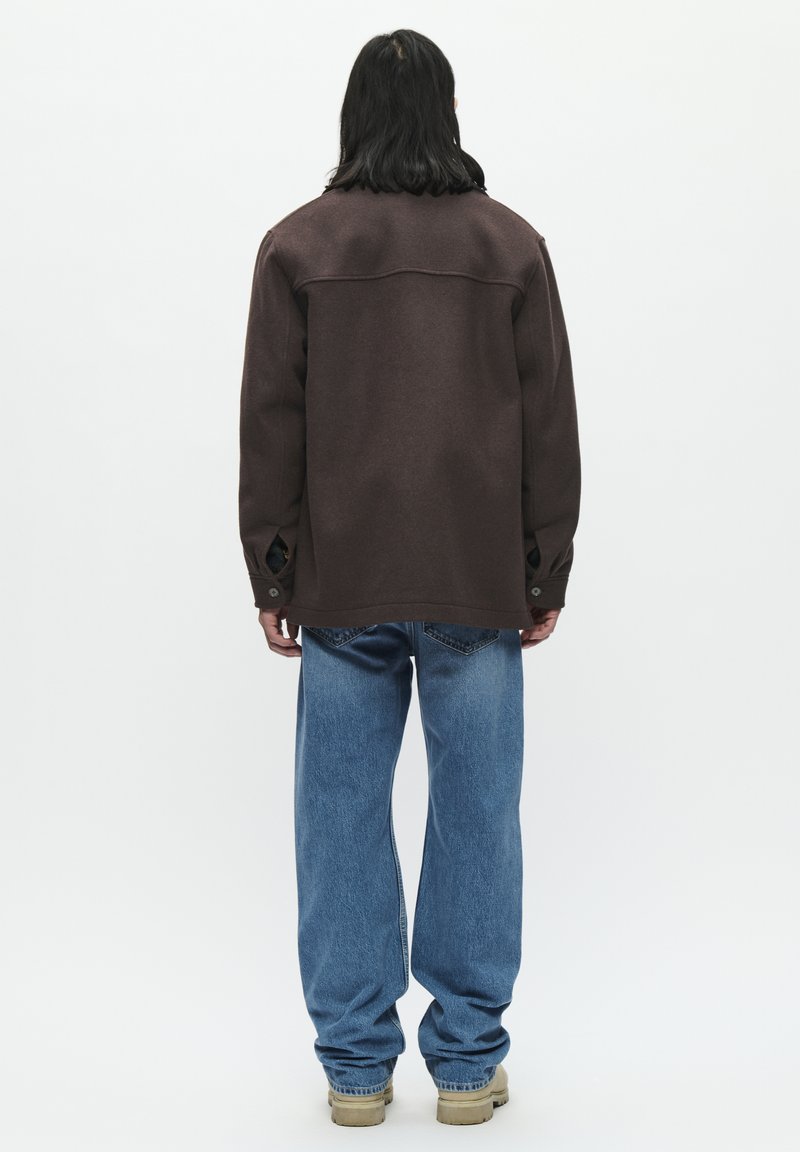 Bruine lange mouw shirtjack met een relaxte pasvorm, voorzien van een gladde textuur, knoopmanchetten en blauwe wijde jeans met een vervaagd uiterlijk.