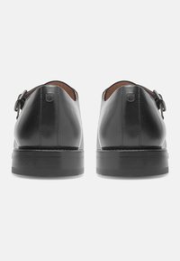 Chaussures en cuir noir au design élégant, avec un bout rond et un accent à double boucle. Talon plat avec une semelle texturée pour une meilleure adhérence.