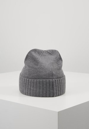 Bonnet en tricot gris avec bord-côte présenté sur un cube blanc sur fond gris clair uni.