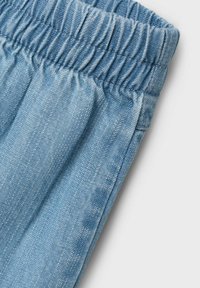 Tessuto denim azzurro chiaro con una cintura elastica, caratterizzato da una texture liscia e un sottile effetto sbiadito, inclinato per mostrare i dettagli.