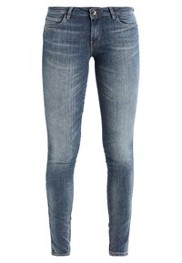 Jeans ajustados en denim azul medio con un leve desgastado, cinco bolsillos y cierre con cremallera. Presenta un pequeño acento metálico en la cintura.