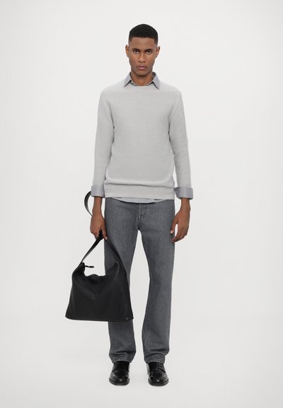 Grau strukturierter Pullover, hellblaues Hemd mit Kragen, dunkelgraue Jeans, schwarze Tasche, schwarze Schuhe. Model steht zentral vor einem weißen Hintergrund.