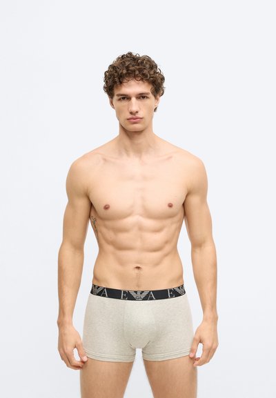 Beżowe bawełniane spodenki z czarną, markową elastyczną talią. Tkanina ma gładką teksturę, dopasowany krój i długość do połowy uda.