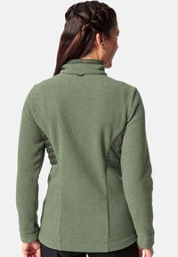 Groene fleecejas met een getextureerde afwerking, voorzien van een gladde gegarneerde panel op de achterkant en een hoge kraag. Accenten omvatten een klein logo.
