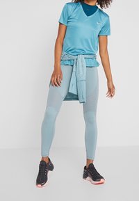 Ljusblå träningströja med v-ringning, i kombination med matchande leggings som har texturerade paneler. Svarta och rosa träningsskor fulländar outfiten.