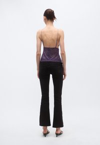 Lilla kirju mustriga varrukateta topp avatud seljaga, õhukeste rihmade ja pitsäärega, kokku sobitatud mustade lõhenevate teksadega.