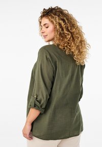 Chemise légère olive, à manches roulées, dotée d'un détail de bouton et d'un tissu texturé. La vue arrière met en avant la coupe décontractée et le tombé.