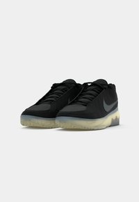 Čierne športové tenisky s textúrovaným vrchom, jednoducho navrhnuté a s priehľadnou gumovou podrážkou. Obsahuje bočné logo Nike swoosh.