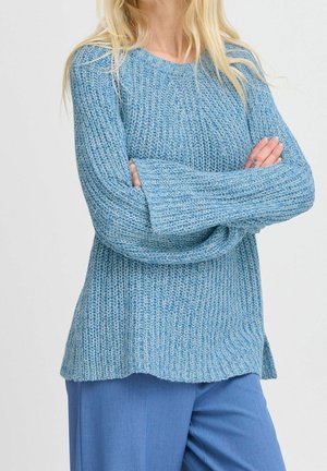 Lichtblauw gebreid trui met lange mouwen, geribbelde textuur en zijsplitten. Gekleed met bijpassende blauwe broek.