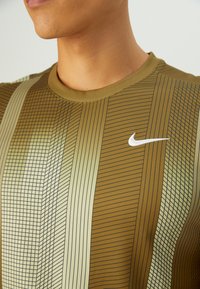 Olivengrønn Nike sportskjorte med vertikale stripemønstre i forskjellige nyanser, med en liten hvit Nike-logo på brystet.