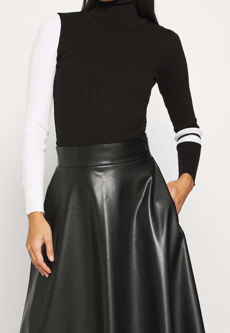 Pull à col roulé côtelé noir et blanc avec des manches longues contrastées et une coupe ajustée, associé à une jupe en cuir noir brillant.