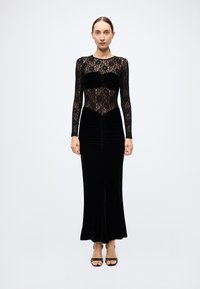 Black dress featuring a lace long-sleeve bodice and velvet skirt with gathered details. The silhouette is form-fitting and elegant.