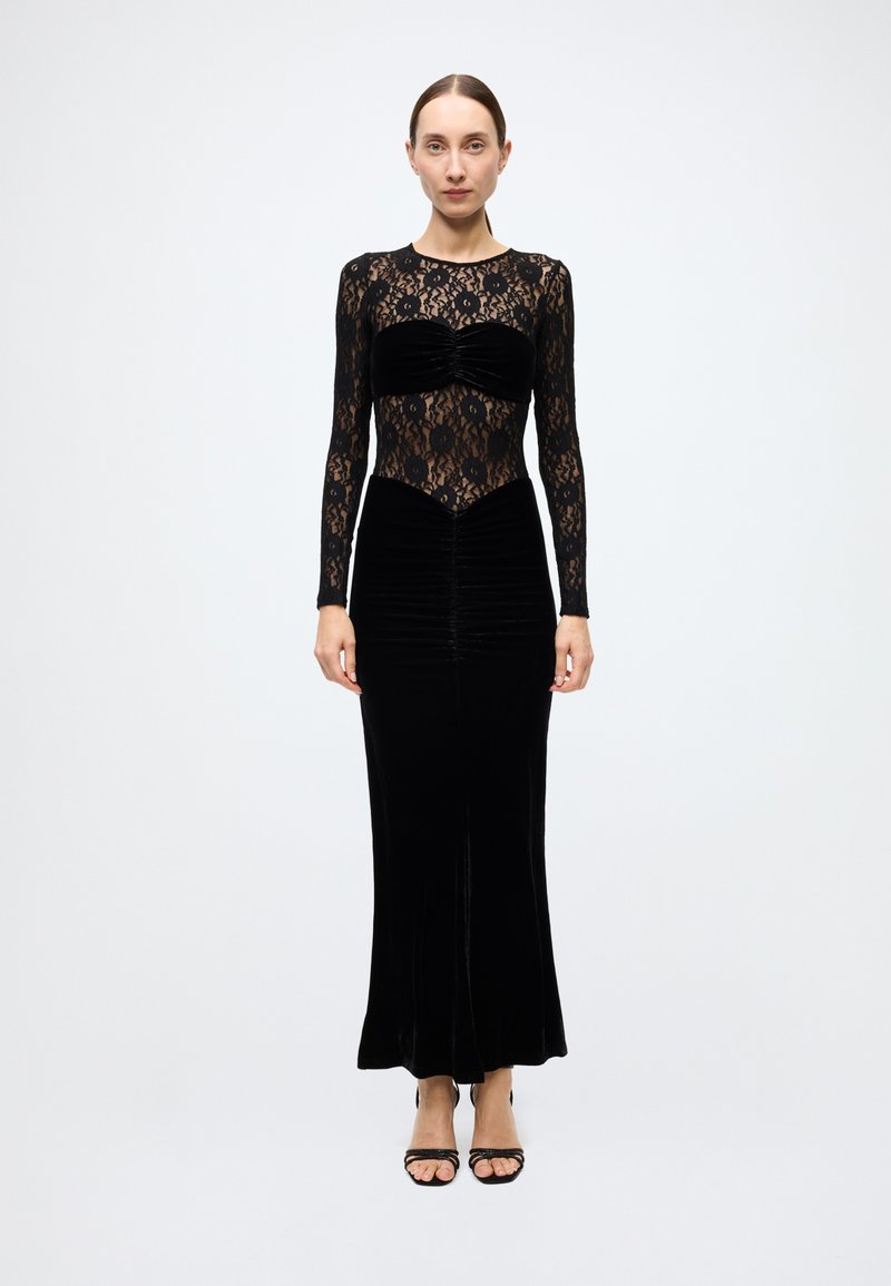Black dress featuring a lace long-sleeve bodice and velvet skirt with gathered details. The silhouette is form-fitting and elegant.