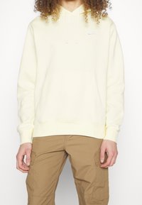 Ljusgul hoodie med en framficka, justerbar dragsko på huvan och liten vit Nike-logga på bröstet. 100% bomull.