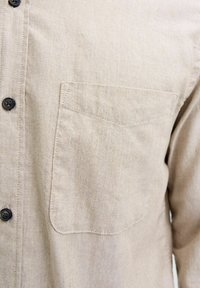 Beige button-up shirt with a single chest pocket on the left side, detailed stitching, and dark buttons.