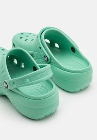 Mintgrønne Crocs-kloger med lukket hæl, perforeringer for ventilasjon og en teksturert fotseng. Sålen er tykk og slitesterk.