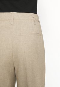 Pantaloni beige a motivo spina di pesce con tasca posteriore. Tessuto misto cotone, forma sartoriale con vita a media altezza, superficie lavorata.