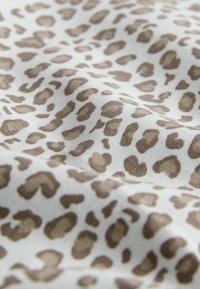 Tejido de estampado de leopardo que presenta un fondo blanco con manchas marrones irregulares. La textura parece tejida y ligeramente rugosa.