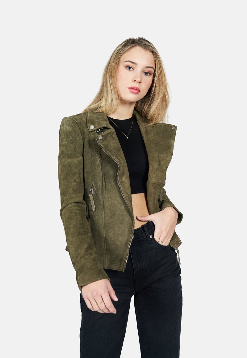 Olijfgroene suède motorjack met een asymmetrische rits, ritszakken en een getailleerd silhouet. Gecombineerd met zwarte high-waisted jeans.