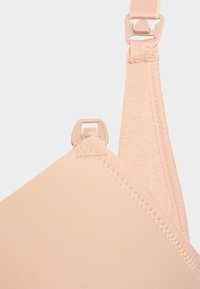 Mjuk beige behårem med kupa, detaljerad sömnad och plastspänne för justering på ljus bakgrund.