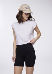 T-shirt corta bianca a maniche corte abbinata a short da ciclista neri a vita alta. Un cappellino beige con "NEW YORK" ricamato sulla parte anteriore.