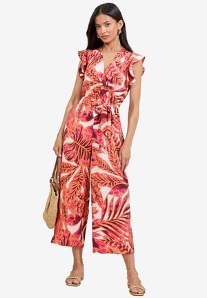 Jumpsuit stampato floreale in toni di rosa e arancio, caratterizzato da maniche a volant, vita con cintura e design a gamba larga. Indossato con una borsa intrecciata.