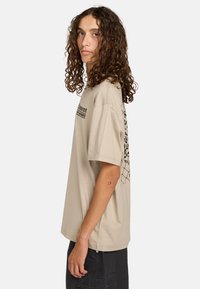Beige short-sleeve t-shirt made of cotton with a loose fit, featuring black graphic print on the left sleeve and the front chest area.