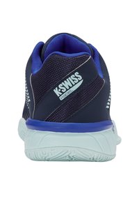 Aizmugures skats uz tumši zilā un purpursarkanā K-Swiss Padel sporta apavu modeli ar biezu baltu zoli un kokvilnas auduma detaļām.