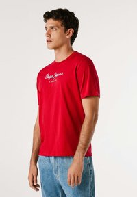 Rdeča bombažna majica s kratkimi rokavi in krojnim ovratnikom, z belim logotipom "Pepe Jeans London" na sprednji strani ter sproščenim krojem.