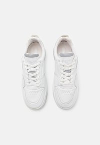 Sneaker bianche in pelle con texture liscia, collo imbottito, punta perforata e design con lacci, caratterizzate da sottili accenti grigi e branding.