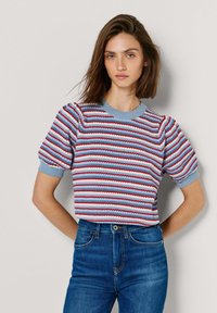 Gestreifter Pullover mit kurzen Ärmeln in Blau, Rot und Weiß, mit gerippter Struktur und wellenförmigem Ausschnitt. Kombiniert mit hoch taillierten Jeans.