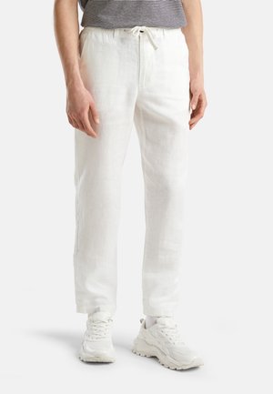 Persona que lleva pantalones de lino blancos con cordón, zapatillas blancas gruesas y una camisa a rayas negras y blancas.