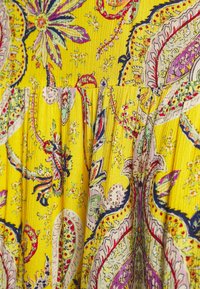 Tela amarilla con intrincados patrones florales y paisley en púrpura, rosa y verde, con un acabado texturizado y plisado.