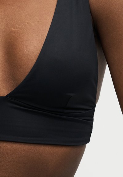 Gros plan sur le torse d'une personne portant un haut noir sans manches à col en V profond, sur fond clair.