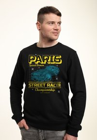 Felpa nera con grafica di un'auto blu e testo giallo che recita "PARIGI" e "Campionato STREET RACER". Vestibilità casual con scollatura rotonda.