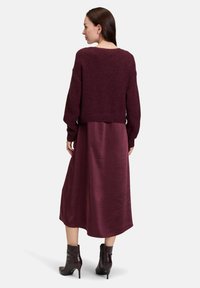 Pull en tricot bordeaux à coupe courte et manches longues, associé à une robe fluide bordeaux. Des bottines à la cheville complètent la tenue.