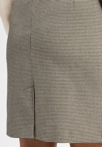 Schwarz-weißer Rock im Hahnentritt-Muster, knielang mit geradem Schnitt und Seitenschlitz, aus strukturiertem gewebtem Stoff.