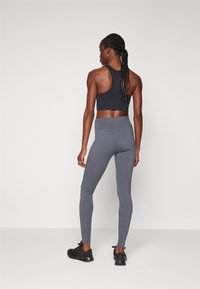 Svart sportsbh med racerback-design kombinert med grå høyhalsede tights. Modellen har på seg svarte joggesko.