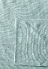 Ljusblå strukturerad stickad tyg med en stor fickdetalj. Mönstret är enhetligt och visar det mjuka, andningsbara materialet.