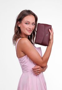 Burgundské kožené psaníčko s překlopnou klopou, zdobené švy podél okrajů a jemným logem. Hladký povrch a obdélníkový tvar.