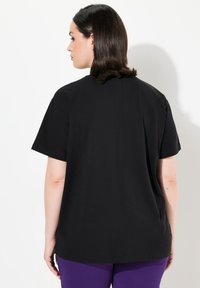 Musta lyhythihainen t-paita rennolla leikkauksella ja pyöreällä kaula-aukolle, valmistettu pehmeästä puuvillakankaasta. Takana on yksinkertainen suunnittelu.