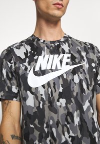 Grå kamouflage t-shirt i bomull, med en djärv vit Nike-logga över bröstet. Korta ärmar och rund halsringning.