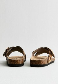 Bruine en beige luipaardprint sandalen met een kurken voetbed, verstelbare riem en zwarte rubberen zool, bekeken van achteren.