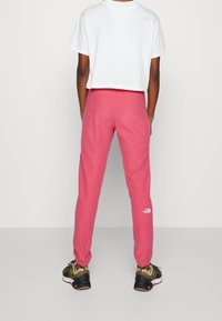 Růžové tepláky s elastickými manžetami, na levé noze s bílým logem. V kombinaci s bílým zkráceným tričkem a sportovními botami.