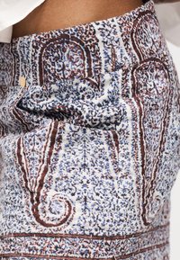 Κοντινό πλάνο υφάσματος με περίτεχνα καφέ, μπλε και λευκά μοτίβα πεϊσλεϊ και λουλουδιών σε εφαρμοστά παντελόνια.